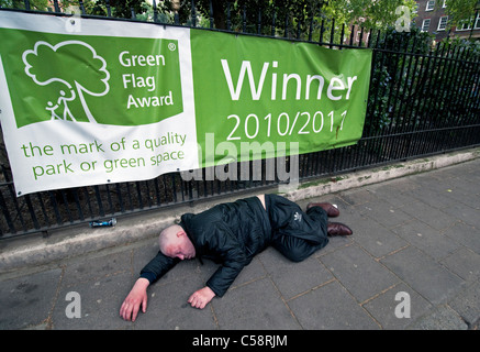 Drunken man lying on pavement asleep in the street in front  of ironic sign Stock Photo