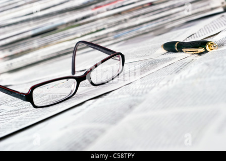 reading glasses and a ballpoint pen lie on a newspaper Stock Photo