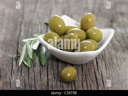 Green olives in the bowl and olive branch on wooden table Stock Photo