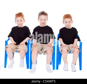 Three boys sitting on blue chairs on white Stock Photo