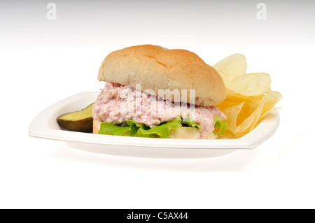 Ham salad with lettuce sandwich in a roll with potato chips and  a pickle on white plate on a white background, cut out. Stock Photo