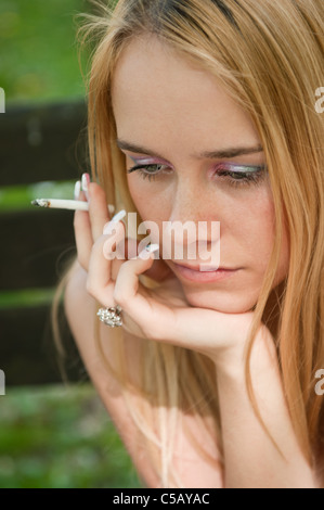 Lifestyle portrait of young worried and depressed woman smoking cigarette outdoors Stock Photo