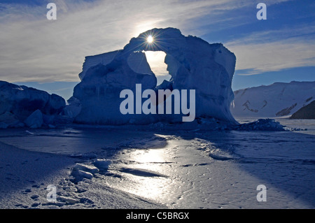 Sun shines through hole in iceberg arch set in sea ice in Ross Sea Antarctica Stock Photo