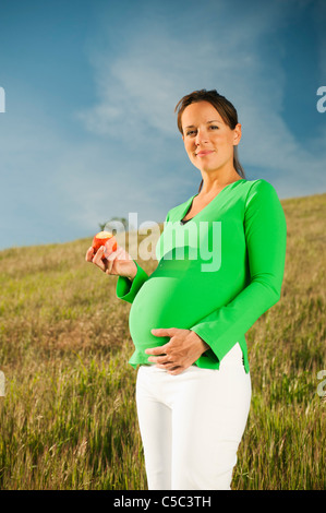Pregnant Hispanic woman eating apple in field Stock Photo