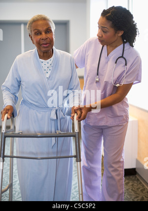 Nurse helping woman use walker in hospital hallway Stock Photo