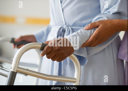 Nurse helping woman use walker in hospital hallway Stock Photo