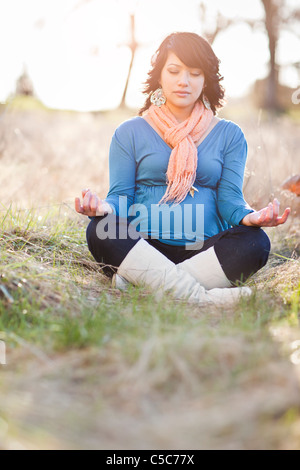 Pregnant mixed race woman practicing yoga in field Stock Photo