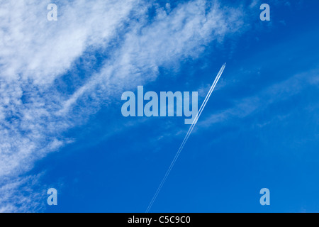 A passenger aircraft in Britain leaving vapour trails against a blue sky and high cloud Stock Photo