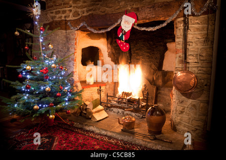 Inglenook fireplace in old house with high blazing log fire and decorated Christmas tree, stocking and copper kettle. JMH5161 Stock Photo