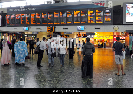 Euston railway train station concourse back view traveller passengers viewing train departure information board shops beyond Camden London England UK Stock Photo