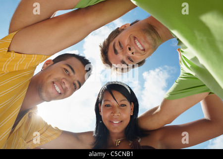 multiethnic group of male and female friends hugging and looking at camera with sky in background. Low angle view Stock Photo