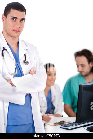 Serious young doctor looking at the camera, two others making notes in the background Stock Photo