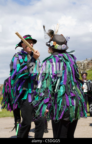 Exmoor Border Mixed Morris Dancers, black-faced, wearing long flowing torn old rags, clothing made from wide bolts of blue and white material, clothes & dancing celebration, outdoors event, street dancer, costumed dancers, performance, folk entertainers, multi colored, music festival, musicians, popular, performing traditional leisure activity at Tutbury Castle Weekend of Dance  Derbyshire, UK.