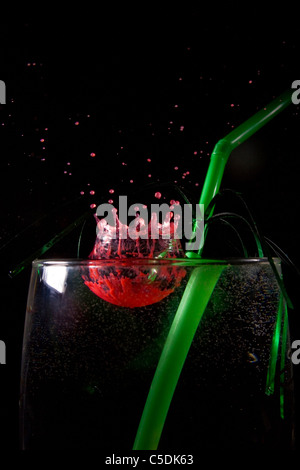 red food coloring being dropped in to a glass of water, with a green drinking straw in the glass. Stock Photo