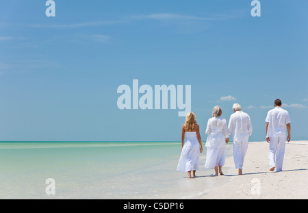 Rear view of four people, two seniors, couples or family generations, holding hands, walking on a tropical beach Stock Photo