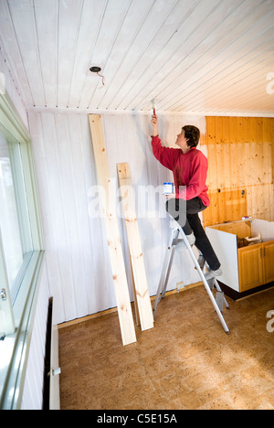 Side view of a woman painting the ceiling at home
