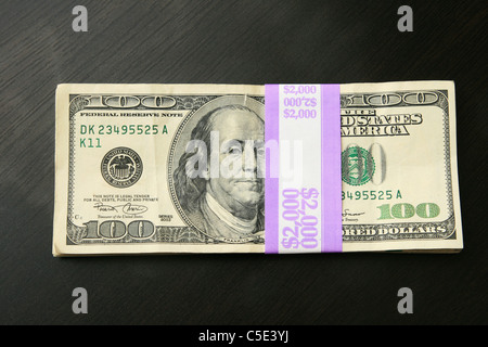 two thousand dollars in 100 bills on a dark wood table top Stock Photo