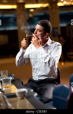 man sitting by the slot machine, lighting confident a cuban cigar Stock Photo