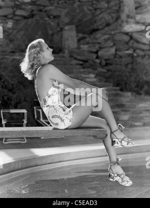 Smiling woman sitting on edge of diving board Stock Photo