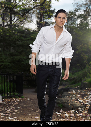 License and prints at MaximImages.com - Photo of a stylish young man walking through a park in the evening Stock Photo
