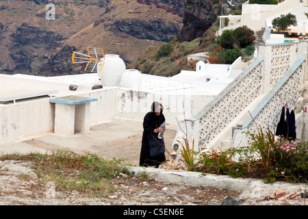 Thira, Santorini, Greek Island, Greece, Europe old lady wearing all black in mourning holding water bottle Stock Photo