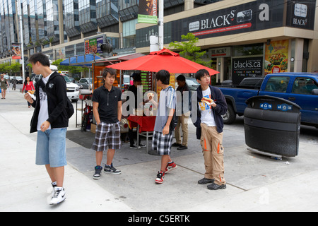 group of young asian men eating hotdogs bought from on street hot dog vendor downtown toronto ontario canada Stock Photo