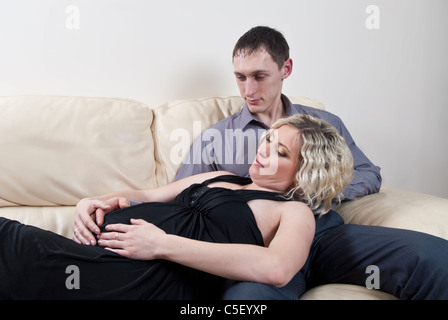 Pregnant couple sat on sofa Stock Photo