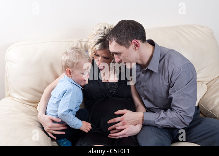 Pregnant woman with her husband and son sat on sofa at home Stock Photo