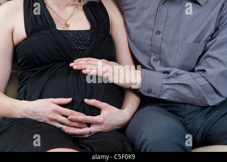 Pregnant couple sat down on sofa Stock Photo