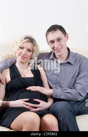 Happy pregnant couple sat on sofa Stock Photo