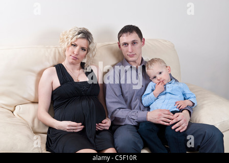 Pregnant woman with her family sat on sofa Stock Photo