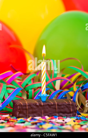 a burning candle on a small cake with streamers and balloons Stock Photo