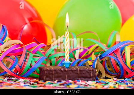 a burning candle on a small cake with streamers and balloons Stock Photo