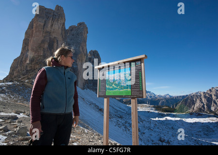 Female hiker looking at map display in front of Tre Cime di Lavaredo, Sexten Dolomites, Italy Stock Photo