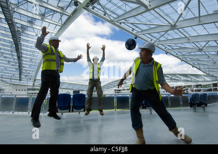 Three builders having a kickabout as work nears completion on the new AMEX stadium, home of Brighton and Hove Albion from 2011. Stock Photo