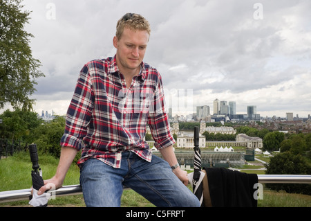 Photo of one modern Millennial man sitting on the fence looking pensive with a view from the Observatory beyond. Greenwich London England UK Britain Stock Photo