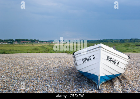 Boat on shingle beach at Cley-next-the-Sea, Norfolk, UK, with salt marshes behind and Cley windmill and village in distance Stock Photo