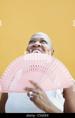 portrait of african 50 years old woman with bald head and fan smiling on yellow background. Stock Photo