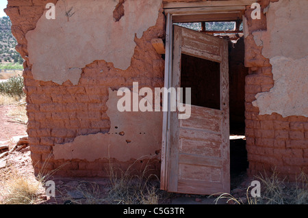 A door leans inward on an abandoned house in Cuervo, New Mexico. The mud brick beneath the cracking adobe facade is visible. Stock Photo