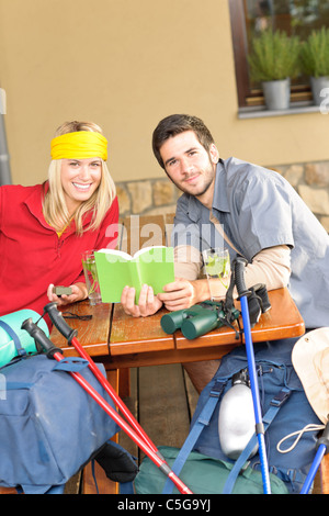 Tramping young couple backpack relax sitting by wooden cottage Stock Photo