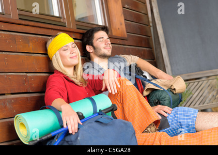 Tramping young couple backpack sleep sitting by wooden cottage Stock Photo