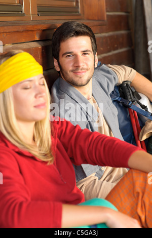 Tramping young couple backpack relax sitting by wooden cottage Stock Photo