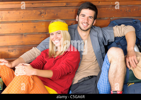 Tramping young couple backpack relax sitting by wooden cottage Stock Photo