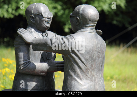 a statue of two bald men wearing sunglasses greeting each other, shaking hands and patting shoulders Stock Photo