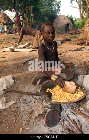 Surma women and girl baking corn and grinding west of Omo River Ethiopia Stock Photo