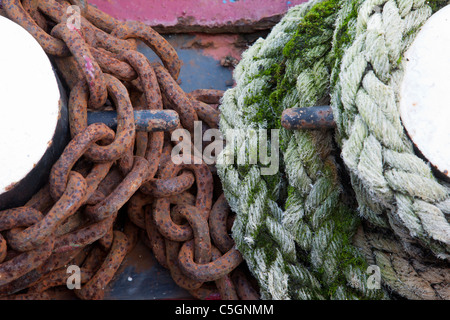 Coils of rusty chain and moss covered rope wrapped around bollards Stock Photo