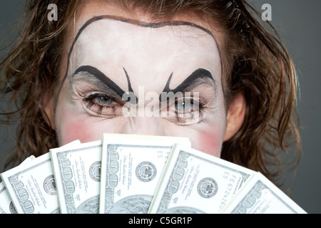 Painted face behind several banknotes Stock Photo