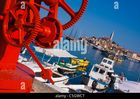 Reed boat crane with sprockets in front of Rovinj fishing boat harbor with the city and blue sky in the background. The motive Stock Photo