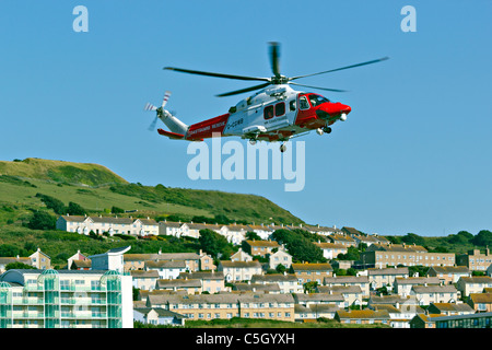 Coastguard rescue helicopter approaching hovering coming into land taking off with Portland in background Stock Photo