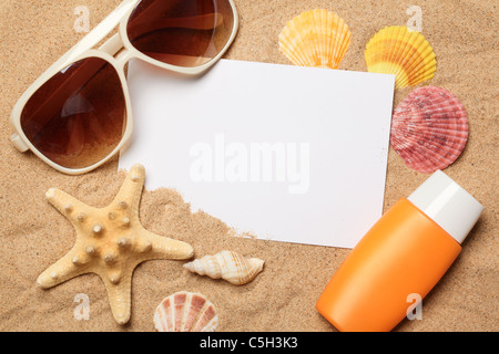 Sunglasses,sunblock and seashells with a blank card on sand. Stock Photo